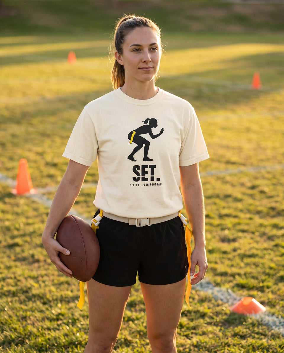 Ivory Set Tee worn by a player holding a football on a field, black crouching silhouette and SET. on chest