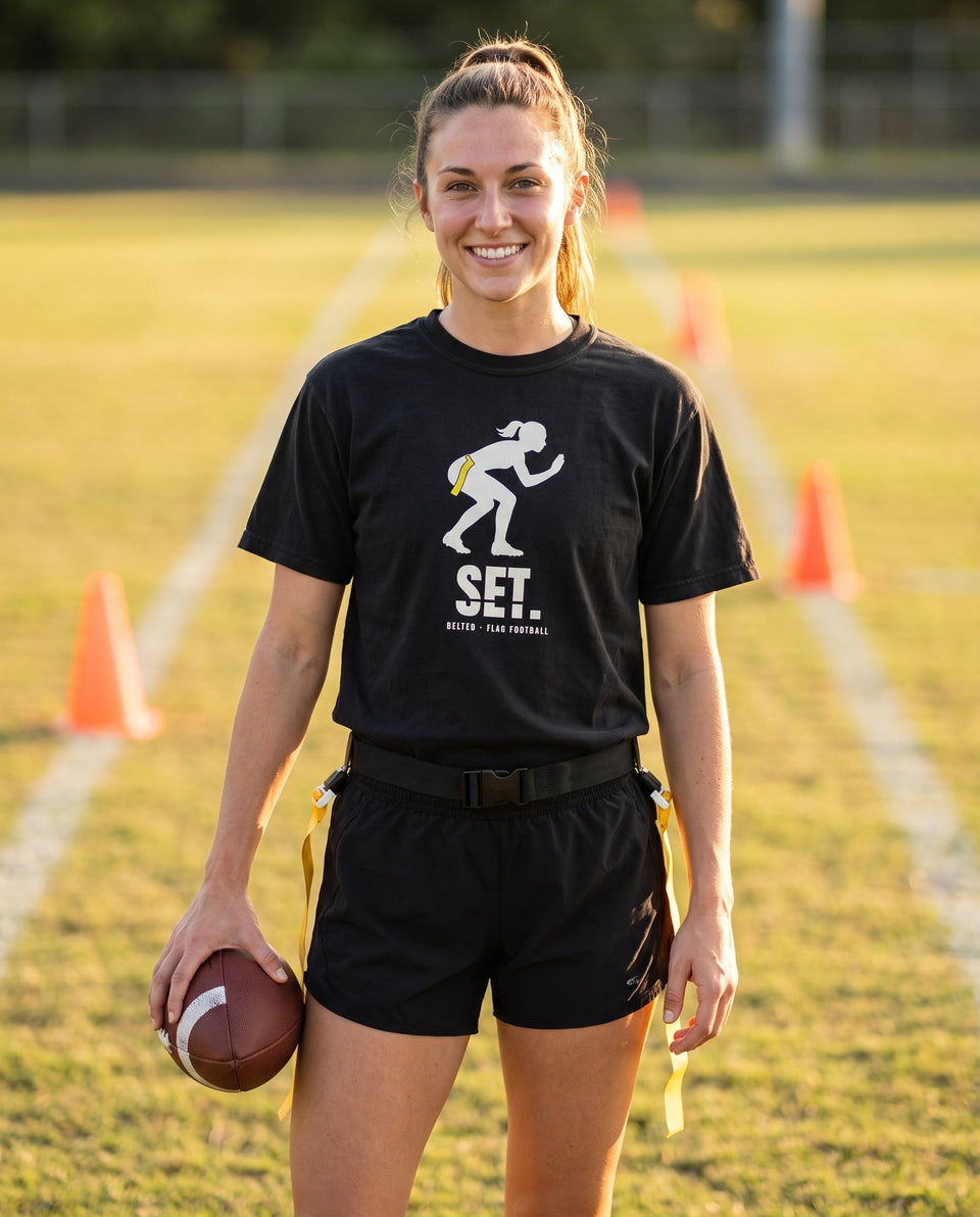 Black Set Tee worn by a smiling player holding a football on a field, Ivory crouching silhouette and SET. on chest