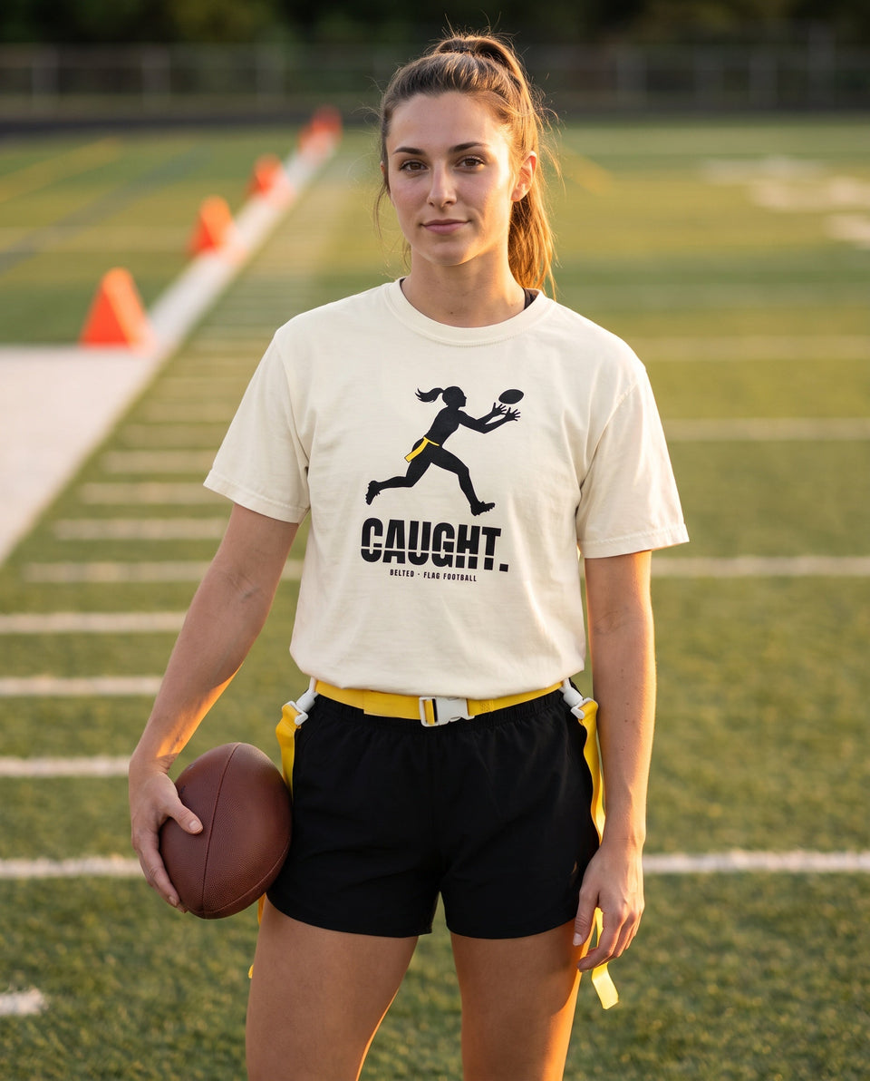 Caught Tee in Ivory, worn by a flag football player with a yellow flag belt on a field, black CAUGHT. print